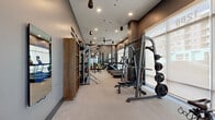Located in Lakewood, Colorado, this modern fitness center offers a comprehensive workout environment designed to accommodate a wide range of exercise needs. The space features a clean, contemporary aesthetic with warm taupe walls, recessed lighting, and stylish pendant fixtures that contribute to an inviting yet functional atmosphere.

Large floor-to-ceiling windows line one side of the facility, flooding the interior with natural light and providing open views of the surrounding neighborhood. Full-length mirrors along the opposite wall visually expand the space and support strength training activities. The light-toned flooring extends throughout, maintaining a cohesive and polished look.

Cardio equipment includes multiple Life Fitness treadmills and stationary bikes, including Echelon smart bikes with integrated screens. The strength training area is well-appointed with a multi-functional cable machine, a power rack with weight plate storage, a dumbbell rack with a full range of free weights, and an adjustable bench. A dedicated functional training zone features TRX suspension straps, resistance bands, and a stability ball.

A separate frosted-glass enclosed room provides a private space for focused training or cycling sessions. Built-in open shelving with wooden accents adds warmth and organizational storage. Ceiling fans ensure comfortable airflow throughout. This fitness center delivers a professional-grade workout experience in a refined, well-lit setting.