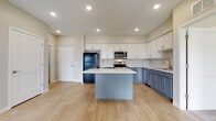 This well-appointed single-floor unit offers a thoughtfully designed open-concept layout that seamlessly connects the kitchen and living areas. The kitchen is a standout feature, showcasing a two-tone cabinetry scheme with crisp white upper cabinets and slate-blue lower cabinets, complemented by bright white countertops and a central island. Stainless steel appliances, including an electric range, over-the-range microwave, and dishwasher, are paired with a black refrigerator for a stylish contrast. Light wood-tone flooring runs throughout the main living areas, enhancing the airy, contemporary feel. The living room is spacious and bright, featuring a ceiling fan and sliding glass doors that open to a private balcony, inviting natural light and outdoor views. Two generously sized bedrooms are finished with plush carpet and multiple windows that frame neighborhood views, creating comfortable, light-filled retreats. The unit includes two bathrooms, each featuring light wood flooring, gray shaker-style vanity cabinetry, white countertops, and brushed nickel fixtures. One bathroom includes a walk-in shower, while both offer clean, modern finishes throughout. Overall, the unit presents a cohesive, contemporary aesthetic with neutral tones and quality finishes.