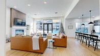 Located at 20021 Chad Hittle Dr in Westfield, Indiana, this thoughtfully designed single-floor community space offers a generous layout across a well-appointed floor plan. The open-concept living room is a standout centerpiece, featuring warm hardwood-style flooring, recessed lighting, and floor-to-ceiling black-framed glass doors and windows that flood the space with natural light and frame sweeping views of the outdoor pool area. A striking accent wall with an arched geometric wallcovering adds a refined, artistic touch to the lounge area, which is furnished with comfortable seating around a welcoming fireplace. The kitchen is both functional and stylish, showcasing slate-gray shaker cabinetry, a marble-tiled backsplash, crisp white quartz countertops, and a large central island with bar seating for multiple guests. Sleek black pendant lights hang above, complementing the modern aesthetic. A dedicated office features dual windows with roller shades, offering a bright and focused work environment with outdoor views. A unique golf simulator room with turf flooring, a projection screen, and an adjacent lounge area provides a recreational amenity unlike any other. Multiple hallways connect the zones seamlessly, creating a smooth and intuitive flow throughout the entire space.