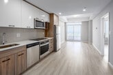 Located on the 29th floor of a contemporary high-rise at 20 George Street in downtown Hamilton, this two-bedroom, two-bathroom unit offers a well-designed layout with a bright, modern aesthetic throughout. Light wood-toned flooring runs continuously across the entire floor, complementing the neutral warm-grey walls and clean white trim that define the interior palette.

The open-concept living and kitchen area is anchored by large floor-to-ceiling sliding doors that lead to a balcony, flooding the space with natural light and offering expansive views of the Hamilton cityscape and the Niagara Escarpment beyond. The kitchen features warm wood cabinetry with dark hardware, stainless steel appliances, and a practical layout that integrates seamlessly with the living area.

Both bedrooms are generously proportioned, with large windows that frame sweeping elevated views of the city and surrounding greenery. The primary bedroom includes a built-in wood-toned wardrobe with sleek black handles, providing ample storage. Each bedroom benefits from an abundance of natural light thanks to the high-rise positioning.

The two bathrooms are finished to a clean, contemporary standard. One features a glass-enclosed walk-in shower with a wood-accented vanity and quartz countertop, while the second includes a soaker tub with full white tile surround. Both are bright and neatly appointed.