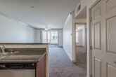 This single-floor residence offers a well-designed, open-concept layout that seamlessly connects the kitchen and living areas. The kitchen is appointed with warm honey-toned wood cabinetry, granite countertops, and a full suite of stainless steel appliances, including a range with over-the-counter microwave and a dishwasher. A peninsula counter provides a natural dividing point between the kitchen and the expansive carpeted living area, which is bathed in natural light streaming through a sliding glass door that opens to a private balcony. Ceiling fans are present throughout the main living space, ensuring comfortable air circulation. The bedroom is generously sized with plush carpeting and dual windows fitted with blinds that allow for adjustable natural light and views of the surrounding exterior. The bathroom features the same granite countertop detailing seen in the kitchen, complemented by warm wood cabinetry, a single-basin sink, and clean tile flooring. Throughout the residence, neutral tones on the walls and trim create a bright, cohesive aesthetic. The overall ambiance is clean, functional, and move-in ready, offering a comfortable and practical living environment.
