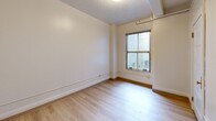 Located at 623 Southwest Park Avenue in Portland, Oregon, this two-bedroom, one-bathroom unit offers a thoughtfully arranged single-floor layout. Light wood flooring runs consistently throughout the space, creating a cohesive and clean aesthetic from room to room.

The entrance opens into a narrow hallway lined with white walls, crown molding, and natural light filtering in from a window at the far end. An intercom system is conveniently positioned near the entry. The kitchen features white cabinetry, under-cabinet lighting, a coil-top electric range, and a full-size refrigerator — all efficiently arranged in an L-shaped configuration that maximizes use of the available space.

Both bedrooms are bright and simply finished, with white walls accented by a chair-rail molding detail and windows fitted with blinds for light control. The primary bedroom includes a ceiling fan and wall-mounted heating unit. Exposed ceiling beams in one bedroom add a subtle architectural character to the space. Each bedroom benefits from its own closet for dedicated storage.

The bathroom is laid out in a galley style, featuring a single-sink vanity with a marble-style countertop, a full tub-shower combination, and a large mirror. The light wood flooring carries through here as well, maintaining the unit's consistent, clean design language throughout.