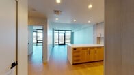 Located in the heart of Hollywood at 1755 Argyle Ave, this contemporary single-floor residence showcases a clean, modern design with an open, airy layout. Light-toned hardwood flooring runs throughout the living spaces, complementing the minimalist aesthetic and bright white walls.

The open-plan living and kitchen area is a standout feature, anchored by a kitchen with warm natural wood cabinetry, a light stone countertop island, and a tiled backsplash. Stainless steel appliances — including a gas range, wall oven, and built-in microwave — complete the well-appointed cooking space.

Floor-to-ceiling windows and glass doors flood the interior with abundant natural light while framing sweeping panoramic views of the Hollywood Hills, the iconic Capitol Records Building, and the surrounding Los Angeles cityscape. These expansive window walls are a defining architectural feature present in multiple rooms, creating a seamless connection between the interior and the vibrant urban environment outside.

The bathroom is finished with marble-look stone surfaces, a wood-framed vanity with an undermount sink, and a glass-enclosed shower. Additional storage is provided by a dedicated walk-in closet with built-in shelving and hanging rods. The unit's elevated position enhances the dramatic views and contributes to a bright, sophisticated atmosphere throughout.