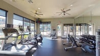 Located at 6800 Gaston Rd in Katy, Texas, this single-floor fitness center is a well-equipped facility designed to support a comprehensive workout experience. The space is bathed in natural light, courtesy of large floor-to-ceiling windows that line the walls and offer views of the outdoor pool area and surrounding lush landscaping, creating an energizing atmosphere for exercise.

The cardio section is generously appointed with multiple treadmills, elliptical machines, and a rowing machine, each equipped with individual display screens for entertainment. Ceiling fans are installed throughout to maintain airflow and comfort during workouts. The strength training area features a full rack of dumbbells and kettlebells in graduated weights, a cable machine, and various resistance equipment, catering to users of all fitness levels.

Full-length mirrored walls on one side of the room amplify the sense of space while allowing users to monitor their form. A bold navy blue accent wall serves as a focal point, adorned with decorative artwork and a wall-mounted flat-screen television. A sturdy workout bench and plyo boxes are also available for functional training. The durable rubber flooring throughout provides stability and safety. Glass doors offer direct access to the outdoor area, seamlessly connecting the interior fitness space with the exterior amenities.