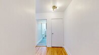 Located at 6001 Chemin de la Côte-Saint-Luc in Hampstead, Quebec, this one-bedroom, one-bathroom unit offers a well-organized layout across a single floor. Warm-toned hardwood flooring runs throughout the living areas and bedroom, adding a classic and inviting character to the space.

The living room is generously sized, bathed in natural light through large black-framed windows that frame views of surrounding greenery. The space flows naturally through a hallway connecting the key rooms. The spacious primary bedroom features multiple windows, including a large picture window overlooking lush trees, paired with a radiator heating system and polished hardwood floors that reflect abundant natural light.

The kitchen is bright and functional, equipped with white cabinetry, ample upper and lower storage, a gas range, refrigerator, and a window overlooking the neighbourhood. Light vinyl flooring complements the clean, all-white aesthetic. The bathroom continues this bright, clean design with marble-style tiled walls surrounding a full soaking tub, a pedestal sink, and light wood-look vinyl flooring. A frosted window provides natural light while maintaining privacy.

The hallway connects all rooms efficiently, completing this well-appointed, move-in ready unit in the desirable Hampstead community.