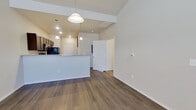 This single-story residence offers a smart, efficient layout with two bedrooms and two full bathrooms. The open-concept living and kitchen area serves as the heart of the home, featuring rich dark wood cabinetry, granite countertops, and black appliances including a range, microwave, and refrigerator. A peninsula with pendant lighting defines the kitchen space while maintaining a seamless flow into the living area. The living room benefits from soaring ceilings that amplify the sense of space, complemented by durable wood-look flooring throughout the main areas. A front entry with notably high ceilings and a large window welcomes natural light into the space. Both bedrooms are carpeted for comfort, with the primary bedroom offering two windows for added natural light and a ceiling fan, creating a bright and airy retreat. The secondary bedroom also includes a window with blinds. Both bathrooms are finished consistently with dark cabinetry, granite-topped vanities, wood-look flooring, and full tub-shower combinations with built-in shelving. The overall aesthetic is clean and contemporary, with neutral tones throughout creating a cohesive and move-in ready environment.