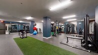 Located at 808 Chapel Street in New Haven, Connecticut, this fitness center offers a generously sized, single-floor facility designed to accommodate a wide range of workout routines. The space features a clean, modern aesthetic with bold blue accent columns, white walls, and durable speckled rubber flooring throughout, complemented by strips of artificial turf that define functional training zones.

The strength training area is well-appointed with a full rack of dumbbells, a power rack loaded with Olympic weight plates, a Smith machine, cable machines, and a dedicated bench press station. Medicine balls and stability balls in multiple sizes are neatly organized near the turf areas, supporting dynamic and core-focused workouts.

The cardio section lines one wall and includes multiple treadmills, elliptical trainers, stair climbers, and stationary bikes, each equipped with individual screens. Floor-to-ceiling mirrors along this wall amplify the sense of space and allow users to monitor their form during exercise.

A TRX suspension training station and functional fitness equipment round out the training options, while a vending machine provides convenient access to snacks and beverages. The facility is brightly lit with recessed and panel lighting throughout, creating a well-illuminated and energizing environment. Restroom access is available on-site, making this a fully self-contained fitness destination in the heart of New Haven.