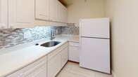 Located at 142 St Marys St in Boston's Fenway neighborhood, this single-floor unit offers a well-organized layout with consistent design elements throughout. The main living area is a standout feature, showcasing warm parquet wood flooring in a classic checkerboard pattern that extends through the space. A large floor-to-ceiling window and sliding glass door open to a balcony, flooding the room with natural light and providing open views of the surrounding Boston cityscape.

The kitchen is efficiently designed with white cabinetry, light stone countertops, a stainless steel sink, and a mosaic tile backsplash in neutral tones. Tile flooring and a full-size refrigerator complete the functional space.

The bedroom continues the parquet flooring theme and includes a generously sized walk-in closet outfitted with shelving and hanging rods, offering ample storage. A separate closet is also accessible from the living area.

The bathroom features classic white subway tile with a contrasting dark border accent, a combination tub and shower, stainless steel grab bars, a white vanity, and mosaic tile flooring—offering a clean, timeless aesthetic throughout.