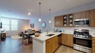 This well-designed single-floor residence showcases a thoughtful open-concept layout that seamlessly connects the kitchen, dining, and living areas into one cohesive and functional space. The kitchen is a standout feature, equipped with warm wood-tone cabinetry, glass-front upper cabinets, a classic white subway tile backsplash, and a full suite of stainless steel appliances including a gas range, microwave, dishwasher, and refrigerator. A peninsula with a sleek white quartz countertop and undermount sink doubles as a breakfast bar, anchored above by stylish pendant lighting. Rich hardwood-style flooring runs throughout the main living areas, adding warmth and continuity. The living room offers a comfortable, welcoming atmosphere with neutral walls, a large window that invites natural light, and ample space for relaxed seating arrangements. The bedroom is carpeted for comfort, features a bright window, and provides generous space for furnishings. The full bathroom is finished with warm wood vanity cabinetry, a white quartz countertop, tile flooring, and a full tub-shower combination. Throughout the space, soft neutral tones, consistent modern finishes, and thoughtful lighting create a cohesive and inviting ambiance.