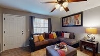 This single-story 2-bedroom, 2-bathroom home offers a thoughtfully designed layout that maximizes functionality across its living spaces. The living room serves as a welcoming focal point, featuring wood-look tile flooring, a ceiling fan with light fixture, and a window dressed with grommet curtains that allow natural light to fill the room. The dining area sits adjacent to the kitchen and living space, providing a seamless open flow ideal for everyday living and entertaining. The kitchen is outfitted with dark espresso cabinetry, light stone-look countertops, a double-basin sink, and white appliances including a range and dishwasher. A dedicated in-unit laundry area with a full-size washer and dryer is conveniently integrated into the kitchen space. Both bedrooms are carpeted and include closets, with the primary bedroom offering a hallway leading directly to its en-suite bathroom. The bathrooms feature dark cabinetry, wood-look tile flooring, and tub-shower combinations with tile surrounds. Neutral gray walls throughout the home create a cohesive, modern aesthetic, while ceiling fans in the main living areas add both comfort and style. Two closets provide ample storage across the floor plan.