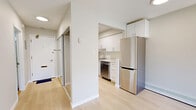 This well-appointed single-floor unit offers a clean, modern aesthetic across three thoughtfully arranged rooms. Light-toned hardwood flooring flows throughout, complementing the crisp white walls and creating a cohesive, airy atmosphere.

The kitchen is a standout feature, outfitted with sleek white cabinetry extending to the ceiling, quartz countertops, a white subway tile backsplash, and a full suite of stainless steel appliances including a refrigerator, electric range, over-the-range microwave, and dishwasher. A stainless steel sink and generous counter space make the kitchen both functional and visually polished.

The living area is bright and generously proportioned, benefiting from large sliding glass doors that open onto a private patio. The patio is enclosed by distinctive decorative concrete block railings and overlooks a tree-lined street, offering pleasant outdoor views and abundant natural light. Baseboard heating runs along the walls throughout the unit, ensuring comfortable year-round temperature control.

An additional room provides a versatile, light-filled space suited for use as a bedroom or office, featuring the same hardwood flooring and neutral tones. A front entry with a closet completes the layout. The unit's clean lines, modern finishes, and natural light create a welcoming and functional living environment.