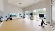 Located at 4359 Sadler Rd in Glen Allen, Virginia, this single-floor amenity center is designed to offer a comprehensive wellness and social experience. The fitness area is expansive and well-appointed, featuring strength machines, free weights, cable equipment, and cardio machines, all set against full-wall mirrors and large windows that invite abundant natural light and outdoor views. A dedicated spin studio provides additional cycling equipment and mirrors, with vaulted ceilings and floor-to-ceiling windows overlooking lush greenery.

An open functional training zone offers ample floor space for group workouts, stability balls, and dumbbell racks, separated from adjacent areas by sleek glass-panel partitions. The social lounge area features warm wood flooring, generous sectional seating, and oversized glass garage doors that open directly to an outdoor patio complete with seating, umbrellas, and string lights. A stylish bar-style seating area with decorative laser-cut metal panels and a shuffleboard table adds a recreational dimension to the space. Dining tables near full-glass walls provide a seamless indoor-outdoor connection. Throughout, the design balances clean modern finishes with inviting, community-focused spaces.