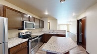 Located at W6399 Sonny Dr in Menasha, WI, this single-floor, two-bedroom residence offers a thoughtfully designed layout with a comfortable and functional living environment. The entrance opens into a kitchen that serves as the heart of the home, boasting rich dark-wood cabinetry, granite countertops, a central island for additional prep space, and a full suite of stainless steel appliances including a refrigerator, electric range, microwave, and dishwasher. The kitchen flows seamlessly into the living area, which is finished with light wood-tone laminate flooring and features a sliding glass door that floods the space with natural light and provides direct access to a lush, green outdoor area. The spacious primary bedroom is carpeted for comfort and includes a ceiling fan, a window with outdoor views, and baseboard heating. The second bedroom is also carpeted and features a large sliding-door closet with rich wood paneling, a baseboard heater, and natural light from a window. Warm neutral tones, dark wood trim, and baseboard heating are consistent throughout, lending the space a cohesive and inviting ambiance. A dedicated closet provides additional storage to complete this practical and comfortable home.