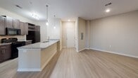 Located at 3340 Shipley St in Ladson, South Carolina, this single-floor unit offers a thoughtfully designed layout that balances functionality and modern style throughout. The kitchen serves as a focal point, featuring rich dark wood cabinetry, granite countertops, a full suite of black appliances including a range, microwave, and refrigerator, and a peninsula with pendant lighting that opens toward the main living area. Track lighting overhead adds a contemporary touch to the space. Light wood-style flooring flows seamlessly through the kitchen, living room, and hallways, creating a clean and cohesive aesthetic. The living area is generously proportioned, offering ample room for comfortable furnishings, and is enhanced by a ceiling fan and a sliding door that invites natural light and outdoor views. The bedroom continues the warm, neutral palette with plush carpeting underfoot, a ceiling fan with light, and a window fitted with blinds that frame views of the surrounding greenery. The bathroom is well-finished with a walk-in glass-enclosed shower, tile surround with built-in shelving, a dark wood vanity with granite countertop, and wood-style tile flooring. Neutral warm-toned walls throughout the unit create a calm, inviting ambiance well-suited to everyday living.