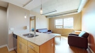 This single-floor unit showcases a contemporary industrial-inspired design, blending modern finishes with functional living spaces. The open-plan kitchen flows seamlessly into the living area, anchored by a granite-topped island with a double stainless steel sink and pendant lighting overhead. Light wood cabinetry, stainless steel appliances — including a range and over-the-range microwave — and warm bamboo-style flooring give the kitchen a clean, practical character.

The living area is generously proportioned, bathed in natural light from a large window that frames sweeping elevated views of the surrounding cityscape. Exposed cylindrical ductwork runs along the concrete ceiling, lending the space a distinct loft-like industrial aesthetic. The room comfortably accommodates a sofa, armchairs, coffee table, and a work desk, making it versatile for both relaxing and working.

The bedroom is a calm, private retreat featuring carpeted flooring, a built-in open closet, and a window that continues the panoramic views found throughout the unit. The bathroom is thoughtfully appointed with a wide vanity featuring a white countertop, undermount sink, light wood cabinetry with brushed metal hardware, and a large mirror. Together, the spaces offer a cohesive, well-designed environment with a balance of industrial character and comfortable modern living.