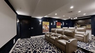 Located at 163 Franklin St in Stamford, CT, this dedicated private screening room delivers an immersive cinematic experience within a thoughtfully designed single-floor space. The room is anchored by rows of plush, tan leather recliner seats with built-in cup holders, arranged in a tiered layout to ensure unobstructed sightlines to the large projection screen mounted at the front of the room. A ceiling-mounted projector provides crisp, high-quality image projection for an authentic theater experience.

The interior design draws heavily from classic Hollywood glamour, with deep navy textured wallpaper featuring a subtle geometric pattern adorning all walls. Vintage movie posters — including iconic titles such as King Kong, Tarzan, Giant, and The Young Racers — are displayed prominently, adding a nostalgic, cinephile character to the space. Sconce lighting along the walls provides warm, ambient illumination that complements the recessed ceiling lights.

A curved, dark wood bar counter with sleek metallic bar stools serves as a social gathering point within the room, accompanied by a cabinetry area housing appliances for snacks and refreshments. The bold black-and-white patterned carpet ties the entire aesthetic together, reinforcing the room's sophisticated yet playful design. This screening room offers an exceptional entertainment amenity for residents of 163 Franklin St.