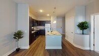 This single-floor residence offers a thoughtfully designed layout that balances comfort and functionality throughout. The kitchen serves as a central highlight, showcasing dark espresso cabinetry, light granite countertops, and a full suite of stainless steel appliances including a range, microwave, and refrigerator. A large kitchen island with a built-in sink and pendant lighting overhead creates an ideal space for both meal preparation and casual dining. Rich hardwood-style flooring runs throughout the kitchen and main living areas, adding warmth and visual continuity.

The bedrooms feature plush carpeting, neutral gray walls, and ceiling fans, contributing to a calm and restful atmosphere. Natural light filters through slatted blinds, brightening each room. The layout provides a clear separation between the living and sleeping areas, offering a sense of privacy.

The bathroom is well-equipped, featuring a dark-toned vanity with granite countertops, a large mirror, and a combination shower and soaking tub enclosed by sliding glass doors. Hardwood-style flooring continues into this space, maintaining design consistency throughout.

A centrally located storage or closet area is visible in the floor plan, offering practical organizational space. Overall, the residence presents a cohesive, modern aesthetic with quality finishes and a functional, open flow.
