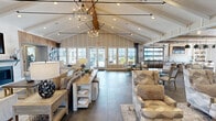Located at 100 Vintage Alcoa Way in Alcoa, Tennessee, this single-story community clubhouse offers a generously proportioned, open-concept living space designed for socializing and relaxation. The interior showcases a modern farmhouse aesthetic, blending warm wood accents, white board-and-batten wall paneling, and large-format stone-look tile flooring throughout.

Soaring vaulted ceilings with exposed beams define the main gathering area, lending an airy, grand ambiance. A welcoming reception nook with natural wood cabinetry serves as a central focal point, while a stone-surround fireplace topped with a wall-mounted TV anchors the comfortable lounge seating area. Curated artwork, including equestrian-themed pieces, adds a distinctive, locally inspired character to the space.

An adjacent dining and bar area features pendant lighting, a full counter with bar seating, open shelving, and an indoor garage-style window that connects to the outdoors. Large multi-pane windows flood the dining zone with natural light and offer views of the surrounding exterior. A semi-private room with glass-panel double doors provides a quieter retreat or meeting space. The entrance foyer, accented with decorative wall sculptures and wicker seating, opens directly to the outdoor patio area, creating a seamless indoor-outdoor flow throughout this thoughtfully designed community hub.