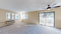 Located at 3834 Northumberland Terr in Fremont, CA, this single-story unit offers a well-organized layout designed for comfortable everyday living. The spacious living area is a central highlight, featuring plush wall-to-wall carpeting, warm beige walls, and a textured ceiling with a ceiling fan overhead. Natural light fills the room through multiple windows fitted with horizontal blinds, while a sliding glass door with vertical blinds opens to an outdoor balcony, providing pleasant views of surrounding greenery. A wall-mounted HVAC unit ensures year-round climate control.

The layout flows naturally from the living area toward a pass-through opening that connects to the galley-style kitchen. The kitchen is outfitted with white cabinetry, light-toned countertops, a gas range with oven, a stainless steel sink, and warm hardwood-style flooring, making efficient use of the available space.

The bedroom areas are carpeted and bathed in natural light from large windows. One bedroom features mirrored sliding closet doors, adding a sense of depth to the room. The bathroom includes a full tub and shower combination with chrome fixtures and hardwood-style flooring, maintaining a clean, functional aesthetic throughout the unit.