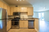 This single-floor residence offers a functional and comfortable layout with a clean, neutral aesthetic throughout. The kitchen is a standout feature, outfitted with a full suite of stainless steel appliances including a gas range, over-the-range microwave, dishwasher, and refrigerator. Light wood cabinetry extends from floor to ceiling, providing generous storage, while granite-style countertops add a polished finish. Track lighting illuminates the workspace, and light hardwood-style flooring ties the kitchen seamlessly into the open living area beyond.

The living area is open and airy, with warm hardwood-style flooring continuing throughout, neutral wall tones, and a peninsula counter that subtly separates the kitchen from the main living space. A secondary room, accessed through a nearby doorway, features plush carpeting and a ceiling fan with a light fixture, along with a window that allows natural light to filter in — making it well-suited as a bedroom.

The bathroom is efficiently designed, featuring a full-size soaking tub with a tiled shower surround, a vanity with a wide mirror and medicine cabinet, and matching light wood cabinetry. Hardwood-style flooring extends into this space as well, maintaining a cohesive look. Overall, the residence presents a tidy, move-in-ready environment with practical finishes throughout.