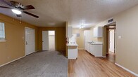 This single-story unit is laid out to maximize functionality across its living spaces. The open-concept living and dining area is finished with wall-to-wall carpet and warmed by golden-yellow walls, with a ceiling fan overhead and windows fitted with horizontal blinds that allow natural light to filter in. The space connects seamlessly to the kitchen area, where the transition to light wood-look flooring marks the boundary between zones.

The galley-style kitchen is efficiently arranged with white cabinetry lining both sides, speckled laminate countertops, a stainless steel sink, and white appliances including a refrigerator and electric range. An overhead panel provides access to utilities, and the layout makes practical use of the available space.

The bedrooms are carpeted and feature ceiling fans, warm neutral walls, and windows with blinds. One bedroom includes a walk-in closet, offering useful storage. Two bathrooms serve the unit, each featuring light wood-look flooring, a white vanity with laminate countertops, and a toilet. One bathroom includes a tiled tub surround. Textured ceilings are consistent throughout the unit, contributing to its practical, understated character.
