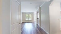 This 840-square-foot, one-bedroom, two-bathroom apartment at Lodge at Foxboro in Foxboro, MA offers a well-designed single-floor layout with consistent wood-look flooring throughout. The living room features crown molding, built-in shelving, an elegant arched entryway connecting to the foyer, and multiple windows that flood the space with natural light and offer views of surrounding greenery. The kitchen is a functional galley-style space with rich dark wood cabinetry, granite-look countertops, and stainless steel appliances including a refrigerator, dishwasher, microwave, and range. The 160-square-foot primary bedroom includes a ceiling fan, a large window with outdoor views, and access to a spacious walk-in closet outfitted with wire shelving and hanging rods. Both bathrooms feature slate-look tile flooring and dark wood vanities with granite-look countertops. One bathroom includes a soaking tub with a tiled surround, while the other offers a tub-shower combination. Three hallways and a dedicated entrance with a paneled door contribute to the apartment's thoughtful flow. The neutral color palette and quality finishes create a clean, modern ambiance throughout this well-appointed residence.
