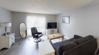 This single-floor residence offers a thoughtfully organized layout across several distinct living spaces. The living room provides a comfortable gathering area with light-toned hardwood-style flooring, a large sliding glass door dressed with vertical blinds that allows natural light to fill the room, and a textured ceiling that carries throughout the unit.

The galley-style kitchen is efficiently designed with dark espresso cabinetry, speckled light countertops, and black appliances including a range, microwave, and refrigerator. Light wood-look flooring and dual-sided counter space make this kitchen both functional and visually cohesive.

The dedicated dining area accommodates a full-sized table with seating for six, centered beneath a ceiling fan with a built-in light fixture, creating a defined space for meals and gatherings.

The bedrooms feature soft carpet flooring, textured ceilings, and neutral wall tones. Mirrored sliding closet doors in the primary bedroom enhance the sense of space, while windows with vertical blinds allow for natural light and privacy control.

The bathroom is laid out with a generous vanity area featuring dark cabinetry, stone-look countertops, and dual mirrors, with a separate water closet and shower area accessible through a private doorway, offering practical separation within the space.