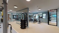This fitness center is a comprehensively outfitted facility designed to support a wide range of workout routines. The space is finished with light, neutral flooring throughout and accented by soft blue-gray walls that create a calm, focused atmosphere. Recessed and flush-mount ceiling lighting ensures the room is evenly and brightly illuminated at all times.

Floor-to-ceiling mirrors line multiple walls, visually expanding the space while allowing users to monitor their form during exercise. The cardio zone is well-stocked with treadmills, elliptical machines, a rowing machine, and a stationary cycling bike, several of which are positioned near windows that offer views of the surrounding exterior, bringing in natural light and a sense of openness.

The free weights area features a full dumbbell rack with an extensive range of weights, ideal for strength training. A Hoist cable machine provides options for resistance-based exercises, while a large functional training rig is equipped with TRX suspension straps, resistance bands, kettlebells, and other accessories — supporting a diverse array of functional and cross-training workouts. The open floor plan allows for ample movement space between equipment zones. Access to the facility is provided through glass-paneled entry doors, contributing to the space's modern, professional aesthetic.