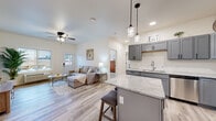 This thoughtfully designed 2-bedroom, 1-bathroom home offers a comfortable and modern living experience across a single floor. The open-concept layout seamlessly connects the kitchen, dining, and living areas, creating a welcoming and functional space. The kitchen is equipped with gray shaker-style cabinetry, stainless steel appliances including a full-size refrigerator, range, microwave, and dishwasher, complemented by light granite countertops and a central island with pendant lighting — ideal for casual dining or meal prep. The living room features light wood-look flooring, a ceiling fan, and large windows that invite abundant natural light. The primary bedroom includes a ceiling fan, a closet, and a window with outdoor views, while the second bedroom is equally bright with plush carpeting and a large window. The full bathroom is finished with gray cabinetry, a tub-shower combination, and wood-look tile flooring. A dedicated laundry room with an in-unit washer and dryer adds everyday convenience. Throughout the home, a neutral, light-toned palette and consistent modern finishes create a clean, cohesive aesthetic that is both functional and inviting.