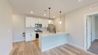 Located at 635 Bay Ave in Toms River, NJ, this single-floor unit showcases a contemporary design with clean lines, light-toned luxury vinyl plank flooring, and a bright, neutral color palette throughout. The open-concept kitchen serves as the centerpiece of the space, featuring white shaker-style cabinetry, quartz countertops with subtle veining, and a geometric tile backsplash. A large center island with an integrated sink and built-in dishwasher provides additional workspace and casual seating. Stainless steel appliances, including a gas range, over-the-range microwave, and refrigerator, complete the kitchen. Pendant lighting with matte black fixtures adds a modern accent above the island.

The kitchen flows seamlessly into the living area, which benefits from generous window placement, allowing abundant natural light and views of surrounding greenery. Bedrooms offer a tranquil retreat; one features light vinyl flooring, while another is finished with plush carpeting, each with large windows framing outdoor foliage.

The bathrooms are well-appointed, with one featuring a subway-tiled tub surround, granite vanity, and matte black fixtures, while another boasts a double-sink vanity with an expansive mirror and matching granite countertop, both finished with neutral floor tiles.