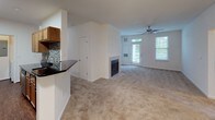 This single-floor residence offers a well-organized layout designed for comfortable everyday living. The open-concept living area serves as the heart of the home, highlighted by a built-in fireplace with a tile surround and a ceiling fan overhead. Large windows and a glass-paneled exterior door flood the space with natural light while providing views of the surrounding greenery. Neutral-toned carpet throughout the living and bedroom areas adds warmth and continuity.

The galley-style kitchen is efficiently designed, featuring dark granite countertops, a stainless steel sink, warm wood cabinetry, a mosaic tile backsplash, and wood-look flooring. A breakfast bar peninsula connects the kitchen to the living area, making the space feel cohesive and functional. A utility area with panel access is conveniently tucked nearby.

The bedrooms are carpeted and bright, each benefiting from natural light through blinds-fitted windows. At least one bedroom includes a standard closet with a rod and shelf. The bathrooms are finished in clean white, each featuring a full tub-shower combination with tiled surrounds, white cabinetry with understated hardware, and square tile flooring, presenting a tidy and practical aesthetic throughout.