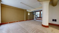 Located at 2058 E. Fourth St. in Cleveland's vibrant E. Fourth Street corridor, this two-floor space blends urban character with functional design. The main level features generously proportioned open living areas with neutral carpet flooring, warm wood baseboards, and exposed ductwork along the ceiling that hints at the building's commercial heritage. Large windows with dark wood frames draw in natural light and offer views of the surrounding cityscape, while structural columns add architectural interest throughout.

A striking metal spiral staircase serves as a central focal point, connecting the two floors with an industrial-modern aesthetic. The galley-style kitchen is efficiently arranged with light wood cabinetry, yellow-toned countertops, tile flooring, and black appliances including a range, refrigerator, and dishwasher.

The upper level continues the carpeted, open layout and includes additional rooms with large windows framing urban views. Rich wood baseboards are consistent throughout. The bathrooms feature tile flooring, white vanities with medicine cabinets, and chrome fixtures. One bathroom includes a soaking tub with surround, while a second provides a full tub-shower combination, completing this well-appointed multi-level space.