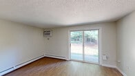 Located at 110 Jobs Hill Road in Ellington, Connecticut, this one-bedroom, one-bathroom unit offers a efficient and well-organized single-floor layout. The living area is a bright, open space finished with warm hardwood-style flooring throughout, neutral light gray walls, and a textured ceiling. A sliding glass door fills the room with natural light and provides outdoor access, while a striking diagonal-planked wood accent wall adds a rustic, architectural focal point that distinguishes the space. A baseboard heating system runs along the perimeter, ensuring year-round comfort. The bedroom is a comfortable, well-proportioned room featuring a large window fitted with blinds that allow for natural light and privacy control. It includes a spacious closet with full-length louvered bifold doors, offering generous built-in storage. Hardwood-style flooring continues seamlessly from the main living area into the bedroom. The bathroom is clean and functional, featuring a white tub-shower combination with tiled surround walls and a chrome towel bar. A hallway connects the rooms, providing a logical and practical flow throughout the unit. The overall ambiance is clean, neutral, and move-in ready, making it a practical living space in a quiet Connecticut town.