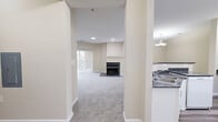Located at 10090 Mill Run Cir in Owings Mills, MD, this single-floor, two-bedroom, four-bathroom residence offers a well-designed layout with comfortable living spaces throughout. The open-concept living and kitchen area serves as the heart of the home, where plush carpeting and neutral warm-toned walls create a welcoming atmosphere. A standout feature is the classic fireplace with a clean white mantle, positioned beneath recessed lighting and alongside sliding glass doors that invite natural light and provide direct access to an outdoor balcony with exterior views. The kitchen is well-appointed with white cabinetry featuring arched detail, dark granite countertops, a peninsula breakfast bar, and white appliances, all set on wood-look luxury vinyl plank flooring. The primary bedroom is generously sized, also with sliding glass door access to outdoor space and carpeted floors. Its en-suite bathroom features a dual-sink white vanity, a large mirror with overhead lighting, and easy access to a walk-in closet with built-in wire shelving. Additional bathrooms are finished with clean white vanities and a tub-shower combination. The space also includes a dedicated hallway, entrance area, and a well-organized closet, combining functionality with a cohesive, understated aesthetic throughout.
