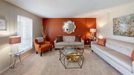 Located at 1401 E Millbrook Rd in Raleigh, NC, this single-floor residence offers a thoughtfully designed layout with a warm, vibrant interior aesthetic. The living room serves as a central gathering space, anchored by a striking burnt-orange accent wall, plush carpeting, and ample natural light from a large window — creating an inviting, energetic atmosphere. Adjacent to the living area, the dining space features wood-look flooring, a pendant light fixture, and a bright window, providing a clean and functional area for meals. The galley-style kitchen is equipped with warm wood cabinetry, a double-basin sink, standard appliances, and a bold teal accent wall that adds a pop of personality. Two bedrooms offer comfortable retreats: the primary bedroom features carpeted floors, a ceiling fan, and generous natural light, while a secondary bedroom includes built-in closet space and room for bunk beds, making it versatile for various living arrangements. The bathroom is finished with wood-look flooring and a shower-tub combination. Throughout the unit, a cohesive color palette of warm neutrals punctuated by teal and orange tones ties each room together, delivering a lively yet functional living environment.