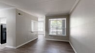 This single-floor residence offers a thoughtfully designed layout with a clean, modern aesthetic throughout. The main living and dining areas are defined by warm hardwood-style flooring, neutral gray walls, crisp white crown molding, and an abundance of natural light streaming through large windows dressed with white horizontal blinds. A pass-through opening connects the living area to the adjacent dining space, enhancing the open flow of the floor plan.

The galley-style kitchen is well-equipped with white shaker cabinetry, light gray laminate countertops, a stainless steel sink, and black appliances including a refrigerator, electric range, built-in microwave, and dishwasher. Light wood-tone flooring continues through this space, complementing the bright, functional layout.

The bedrooms are carpeted in a neutral tone, providing comfort underfoot, and each features ceiling fans, closet access, and windows that bring in natural light. The bathrooms are finished with wood-look tile flooring, gray laminate vanity countertops, white undermount sinks, and brushed nickel fixtures. The full bathroom includes a tiled soaking tub and shower combination with a curved curtain rod and recessed lighting above.

Overall, the space presents a cohesive, move-in-ready interior with consistent neutral tones, practical finishes, and a layout that balances open communal areas with private, well-defined rooms.