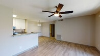 Located at 1700 Green Tree Road in Fredericksburg, Virginia, this single-floor unit offers a clean, modern aesthetic with wood-style flooring flowing consistently throughout the entire space. The open-concept living and dining area is anchored by a ceiling fan with integrated lighting and connects seamlessly to the kitchen via a peninsula counter topped with granite. A sliding glass door floods the living area with natural light and provides outdoor access, while a second ceiling fan adds comfort to the room.

The galley-style kitchen is well-appointed with granite countertops, white upper cabinetry, gray lower cabinetry, and a full suite of stainless steel appliances including a refrigerator, electric range, microwave, and dishwasher. A pendant light above the peninsula adds a polished finishing touch. A pass-through opening connects the kitchen visually to the dining area, enhancing the open feel of the layout.

The bedroom is a quiet, neutral-toned space with a window providing natural light and views of the surrounding greenery. The bathroom includes a full tub-shower combination with a curved curtain rod, wood-style flooring, and grab bar hardware, offering both functionality and practicality throughout.