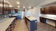 This thoughtfully designed single-floor residence offers a cohesive blend of modern finishes and functional living spaces. The kitchen serves as a standout centerpiece, featuring rich dark cabinetry, granite countertops, a subway tile backsplash, stainless steel appliances including a refrigerator, range, and microwave, and a generously sized island with an undermount sink and pendant lighting overhead. Wood-look luxury flooring flows throughout the kitchen and main living areas, adding warmth and continuity.

The open living room is bright and welcoming, highlighted by a modern fireplace set against a striking accent wall with reclaimed wood-style paneling. Large windows invite natural light and offer views of the surrounding neighborhood and nearby pond.

The bedrooms are carpeted for comfort and equipped with baseboard heating, ceiling fans, and windows that frame outdoor views. One bedroom includes a wall-mounted air conditioning unit for added climate control.

Both bathrooms are finished with granite-topped dark wood vanities and wood-look flooring. The primary bathroom connects directly to a spacious walk-in closet outfitted with wire shelving, while the secondary bathroom features a full tub and shower combination. Throughout, the neutral gray palette and clean architectural lines create a calm, modern ambiance.