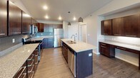 This thoughtfully designed single-floor residence offers a cohesive blend of modern finishes and functional living spaces. The kitchen serves as a standout centerpiece, featuring rich dark cabinetry, granite countertops, a subway tile backsplash, stainless steel appliances including a refrigerator, range, and microwave, and a generously sized island with an undermount sink and pendant lighting overhead. Wood-look luxury flooring flows throughout the kitchen and main living areas, adding warmth and continuity.

The open living room is bright and welcoming, highlighted by a modern fireplace set against a striking accent wall with reclaimed wood-style paneling. Large windows invite natural light and offer views of the surrounding neighborhood and nearby pond.

The bedrooms are carpeted for comfort and equipped with baseboard heating, ceiling fans, and windows that frame outdoor views. One bedroom includes a wall-mounted air conditioning unit for added climate control.

Both bathrooms are finished with granite-topped dark wood vanities and wood-look flooring. The primary bathroom connects directly to a spacious walk-in closet outfitted with wire shelving, while the secondary bathroom features a full tub and shower combination. Throughout, the neutral gray palette and clean architectural lines create a calm, modern ambiance.