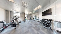Located on Maple Street in Fort Collins, Colorado, this fitness center offers a comprehensive workout environment within a efficiently organized, single-floor layout. The space features a modern design with a drop-panel ceiling, recessed lighting, and neutral-toned carpet tiles laid in a grid pattern throughout.

The cardio section is well-stocked with multiple treadmills, elliptical trainers, upright stationary bikes, and a spin bike, several of which are equipped with personal display screens. Large windows along the perimeter flood the space with natural light while offering views of the surrounding outdoors, creating an open and energizing atmosphere.

The strength training area includes a power rack with an adjustable bench, a barbell, and a full dumbbell rack accommodating a wide range of weights. A wall-mounted flat-screen TV is positioned for visibility across the floor. Full-length mirrors line one wall, visually expanding the space and supporting proper form during exercise.

Additional amenities include wall-mounted yoga mat storage with hooks, a hand sanitizer station, and a glass-panel entry door connecting to an adjacent common area. The overall design is clean, bright, and functional, providing users with a complete fitness facility suitable for both cardio and strength-based training.