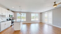 This single-floor residence showcases a thoughtfully designed open-concept layout that seamlessly connects the kitchen, dining, and living areas. Rich hardwood-style flooring flows throughout the main living spaces, complemented by neutral gray walls and recessed lighting that create a bright, welcoming atmosphere. Multiple windows allow abundant natural light to fill the space, offering pleasant outdoor views.

The kitchen is a standout feature, equipped with white shaker-style cabinetry, a subway tile backsplash, gray quartz countertops, and a full suite of stainless steel appliances including a gas range, microwave, and dishwasher. A central island with pendant lighting provides additional workspace and casual seating.

The bedrooms feature plush carpeting and generous closet space, including a walk-in closet with wire shelving in the primary bedroom. The en-suite primary bathroom is elegantly appointed with a double-sink vanity, wood-look flooring, a glass-enclosed walk-in shower with large-format tile, and a separate soaking tub with marble-style tile surround. An additional bedroom includes a standard closet with built-in rod storage, maintaining the unit's consistent, modern aesthetic throughout.