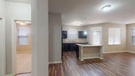 This single-floor residence offers a thoughtfully designed layout that balances comfort and functionality. The open-concept kitchen serves as the heart of the home, showcasing dark espresso cabinetry, light granite countertops, and a suite of black appliances including a refrigerator, microwave, and dishwasher. A central kitchen island provides additional prep space and features a built-in cooktop, illuminated by stylish pendant lighting overhead. Wood-look plank flooring runs throughout the main living areas, lending warmth and a cohesive aesthetic to the space.

The living area flows naturally from the kitchen, providing generous room for entertaining or relaxing. Bedrooms feature plush carpeting, ceiling fans with light fixtures, and window blinds that allow for natural light while maintaining privacy. The primary bathroom includes a dark vanity with a light countertop and a full tub-shower combination, while a secondary bathroom offers a similar design with added accessibility features. A spacious walk-in closet with extensive wire shelving and hanging rods provides abundant storage. Neutral warm-toned walls throughout the home create a calm, inviting atmosphere that complements the consistent design language across every room.