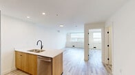 Located at 1800 4th St SW in Calgary's vibrant Mission district, this well-designed one-bedroom, one-bathroom unit offers a thoughtful layout and modern finishes across a single floor. Light-toned, wood-style flooring runs throughout, creating a cohesive and airy feel.

The open-concept kitchen and living area serves as the heart of the unit. The kitchen is equipped with stainless steel appliances, including a full-size refrigerator, stove, and over-the-range microwave. Warm wood cabinetry provides ample storage, while a spacious island with a white quartz countertop and a matte black sink adds both functionality and a contemporary aesthetic. Recessed lighting illuminates the space from above.

The bedroom features a large window with built-in cabinetry below, offering scenic views of the surrounding Calgary cityscape and filling the room with natural light. The clean white walls and light flooring enhance the sense of openness.

The bathroom is finished with an elegant marble-patterned surround enclosing a full soaker tub and shower combination, complemented by crisp white fixtures. A dedicated in-suite laundry area houses a stacked Samsung washer and dryer, adding everyday convenience. The overall ambiance is clean, modern, and functional.