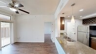 This one-bedroom, one-bathroom unit is thoughtfully laid out across a single floor, offering an efficient and functional living space. Hardwood-style flooring runs throughout, providing a warm, cohesive aesthetic that unifies each area of the unit.

The open kitchen is a standout feature, equipped with stainless steel appliances including a gas range, microwave, and refrigerator. Rich dark wood cabinetry with a wine rack detail adds character, while a granite-topped peninsula with a double stainless steel sink creates a natural division between the kitchen and the dining area. Stylish cone-shaped pendant lights hang above the peninsula, complementing the recessed ceiling lighting throughout the kitchen. A dedicated dining area sits adjacent, illuminated by its own pendant light fixture.

The living area is open and bright, featuring crown molding and a ceiling fan. It connects seamlessly to the bedroom, which includes crown molding, a window with outdoor views, and ample wall space.

The bathroom features a soaking tub and shower combination enclosed by neutral stone-toned tile with a decorative mosaic border accent, lending a polished, spa-like feel. Overall, the unit presents a clean, modern aesthetic with thoughtful finishes throughout.