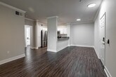 This single-floor unit combines modern finishes with a clean, neutral aesthetic throughout. The living area is a generous, open space highlighted by rich wood-style flooring, crown molding, and a ceiling fan with integrated lighting. A tile-surround fireplace serves as a focal point, while sliding glass doors open directly onto a private balcony enclosed by a metal railing, offering serene, tree-lined views that bring natural greenery into the space.

Adjacent to the living area, the kitchen features an efficient galley-style layout with white shaker cabinetry, gray countertops, stainless steel appliances including a refrigerator, gas range, microwave, and dishwasher, and wood-style flooring that continues the cohesive design. A pass-through counter connects the kitchen to the dining and living areas, enhancing the open feel.

The bedrooms are carpeted for comfort, each equipped with ceiling fans and windows that allow natural light to filter in. The bathroom is finished with a white vanity, gray countertop, an illuminated mirror, and a full tub-shower combination with wood-style flooring completing the space.