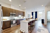 This thoughtfully designed 2-bedroom, 2-bathroom residence combines modern aesthetics with functional living across a single floor. The open-concept kitchen and living area serves as the heart of the home, featuring rich dark-wood cabinetry, quartz countertops, a subway tile backsplash, and a full suite of stainless steel appliances. A spacious kitchen island with bar seating provides an ideal space for casual dining and entertaining, flowing seamlessly into the living area, which is bathed in natural light from large windows dressed with bold navy curtains. Wood-plank flooring runs throughout, adding warmth and continuity to the space. The primary bedroom is generously sized, offering direct access to an en-suite bathroom complete with a dual-sink vanity, dark-wood cabinetry, and a tiled tub-shower combination. A dedicated walk-in closet with wire shelving provides ample storage. The second bedroom is bright and airy, benefiting from large windows and direct access to a well-appointed second bathroom, which also features a dual-sink vanity and tiled shower. Two closets throughout the residence ensure plentiful storage. Recessed lighting, clean white walls, and consistent wood-tone finishes create a cohesive, contemporary ambiance throughout.