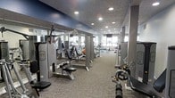 This fitness center is a thoughtfully designed, single-floor facility built to accommodate a wide range of workout needs. The space is outfitted with an extensive array of strength training machines, including cable systems, press stations, and resistance equipment, all arranged to allow comfortable movement between stations. The flooring is covered in durable, textured carpet suited for a gym environment, while the ceiling features recessed lighting that ensures the space is consistently and evenly illuminated throughout. Large windows along one wall allow natural light to filter into the facility, creating a bright and energizing atmosphere. Full-length mirrors are positioned strategically along the walls, enhancing the sense of openness and allowing users to monitor their form during exercises. The interior design incorporates a neutral and professional color palette with dark ceiling accents that lend a modern, polished aesthetic. The layout is open and spacious, with equipment organized in rows to maximize usability and flow. Overall, the facility presents a clean, functional, and well-maintained environment suitable for both casual users and dedicated fitness enthusiasts.