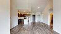 This single-floor residence showcases a thoughtfully designed open-concept layout that seamlessly connects the living, dining, and kitchen areas beneath striking vaulted ceilings. Durable wood-tone luxury vinyl plank flooring runs throughout the main living spaces, adding warmth and visual continuity. The kitchen is well-appointed with dark espresso cabinetry, white quartz countertops, a full suite of stainless steel appliances including a refrigerator, dishwasher, range, and microwave, and a central island with pendant lighting overhead. A solid entry door provides a defined foyer transition into the open living area, which benefits from generous natural light and direct access to a private balcony overlooking open green space. Bedrooms are finished with plush carpeting, ceiling fans, and ample closet space. The primary bedroom connects to an en suite bathroom featuring a glass-enclosed shower, dark vanity cabinetry, and quartz countertops, while a secondary bathroom offers a tub-shower combination with similar finishes. The overall ambiance is clean, contemporary, and move-in ready.