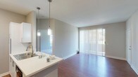 This single-floor residence offers a thoughtfully designed layout that balances comfort and functionality throughout. The open-concept living and kitchen area serves as the heart of the home, featuring warm hardwood-style flooring that extends seamlessly across the main living spaces. The kitchen is well-equipped with stainless steel appliances, including a refrigerator, range, and over-the-range microwave, complemented by white shaker-style cabinetry, light countertops, and a classic tile backsplash. A peninsula with pendant lighting provides additional workspace and connects the kitchen to the living area. The living space is bright and airy, with a sliding glass door fitted with vertical blinds that opens to an outdoor area, allowing natural light to pour in. The bedrooms offer plush carpeting underfoot, neutral gray walls, and ample natural light from well-placed windows, including a charming built-in window seat in one of the rooms. The bathrooms are clean and functional, featuring white vanities with updated fixtures, a tub-shower combination, and wood-style flooring. Throughout the residence, soft neutral tones and clean white trim create a cohesive, modern aesthetic that is both inviting and move-in ready.