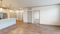 Located at 25 NE Tudor Rd in Lee's Summit, Missouri, this one-bedroom, one-bathroom residence offers a thoughtfully designed layout with contemporary finishes throughout. The open-concept kitchen and living area serves as the heart of the home, showcasing a large quartz-topped island with an undermount stainless steel sink and pendant lighting. The kitchen is fully equipped with stainless steel appliances, including a refrigerator, electric range, and microwave, complemented by a mix of white upper cabinetry, warm wood-toned lower cabinets, and a blue glass tile backsplash. Wood-style plank flooring runs through the main living areas, adding warmth and visual continuity. The living room benefits from natural light through multiple windows and offers access to an outdoor balcony. The bedroom is carpeted for comfort, features a ceiling fan, and includes a generously sized window with outdoor views. The bathroom is finished with a long wood-toned vanity, white quartz countertop, a large mirror, and wood-style flooring, with direct access to the closet. Recessed lighting, neutral walls, and clean architectural lines contribute to a bright, modern, and move-in-ready ambiance throughout the space.